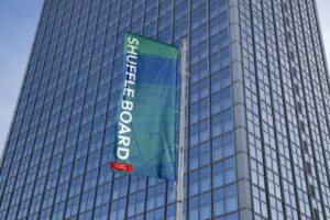 Waving banner that says Shuffle Board, in front of a skyscraper